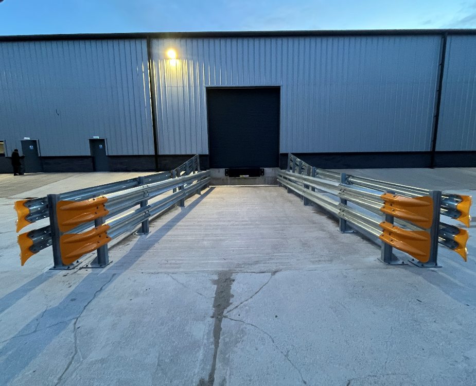 Galvanised Armco crash barriers with orange fishtail ends protecting both sides of a warehouse loading bay door