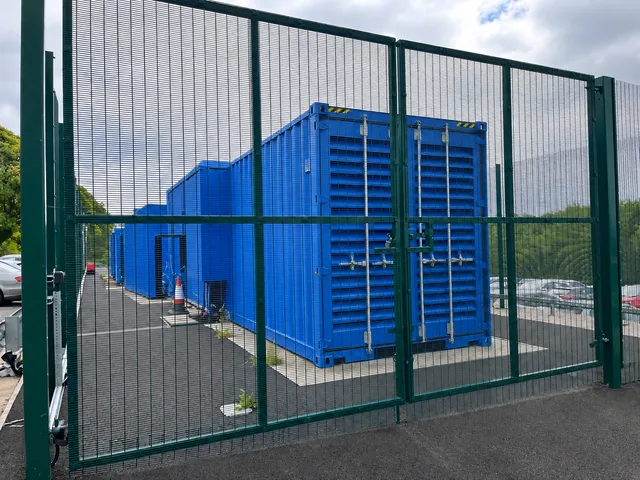 Green mesh double gates securing blue equipment enclosures